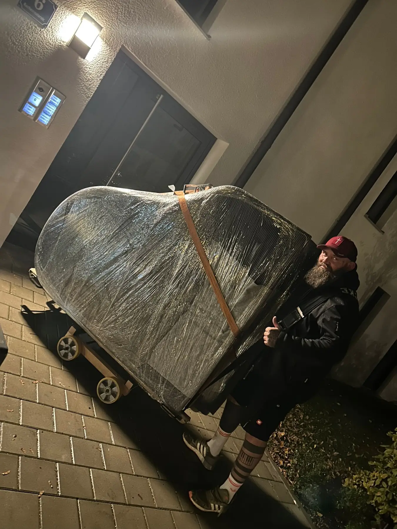 Ein vollständig verpackter Flügel steht auf einem Transportwagen vor einem Hauseingang bei Nacht
