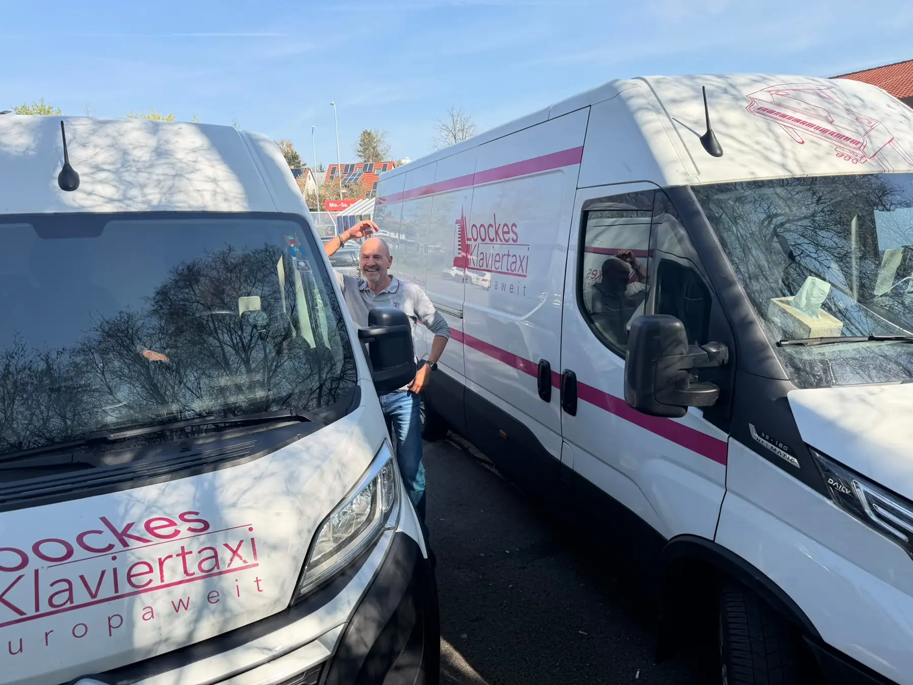 Zwei beschriftete Transporter von Loocke's Klaviertaxi nebeneinander, ein Mitarbeiter mit den Schlüsseln