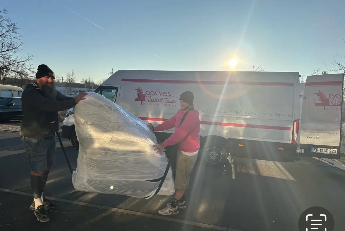 Zwei Mitarbeiter verladen im Morgenlicht einen verpackten Flügel zwischen zwei Lkw